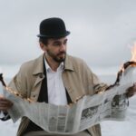 a bearded man reading a burning newspaper
