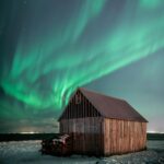 a brown wooden barn under sky with aurora borealis